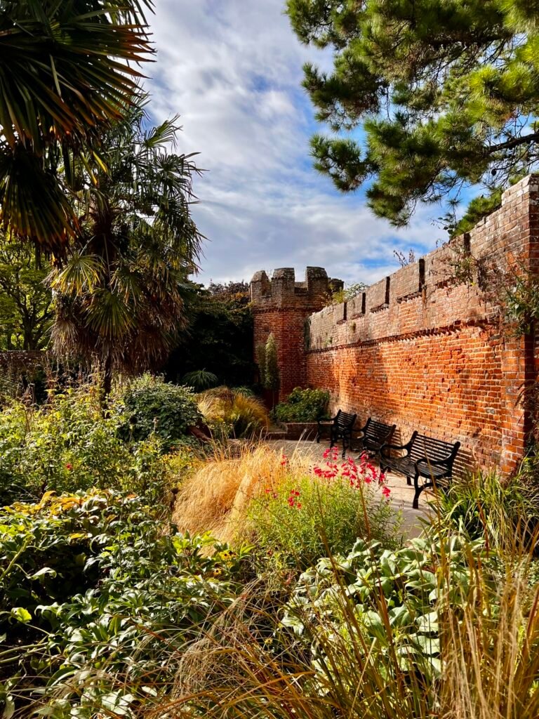 Bishop’s Palace Garden in Chichester with lush planting, benches and historic red-brick wall