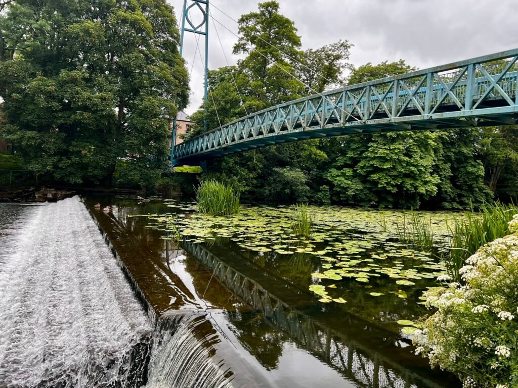 Blue footbridge over the River Stour beside the weir in Blandford Forum