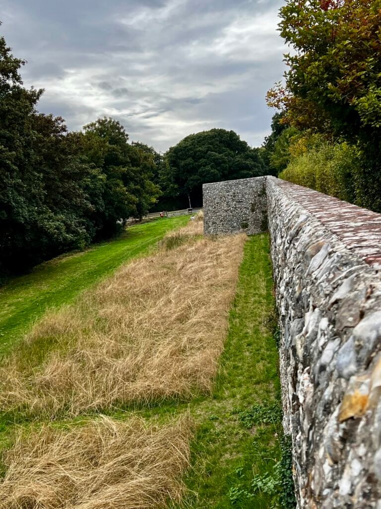 Historic stone and flint section of Chichester city walls beside a grassy path
