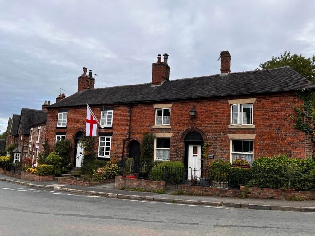 Red-brick village cottages with white windows and an England flag in Astbury, Cheshire.