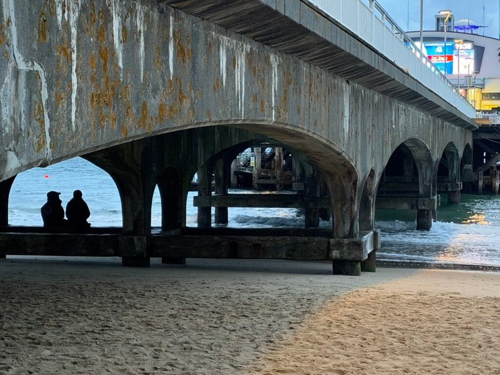 Concrete arches beneath Bournemouth Pier with two silhouetted people overlooking the sea