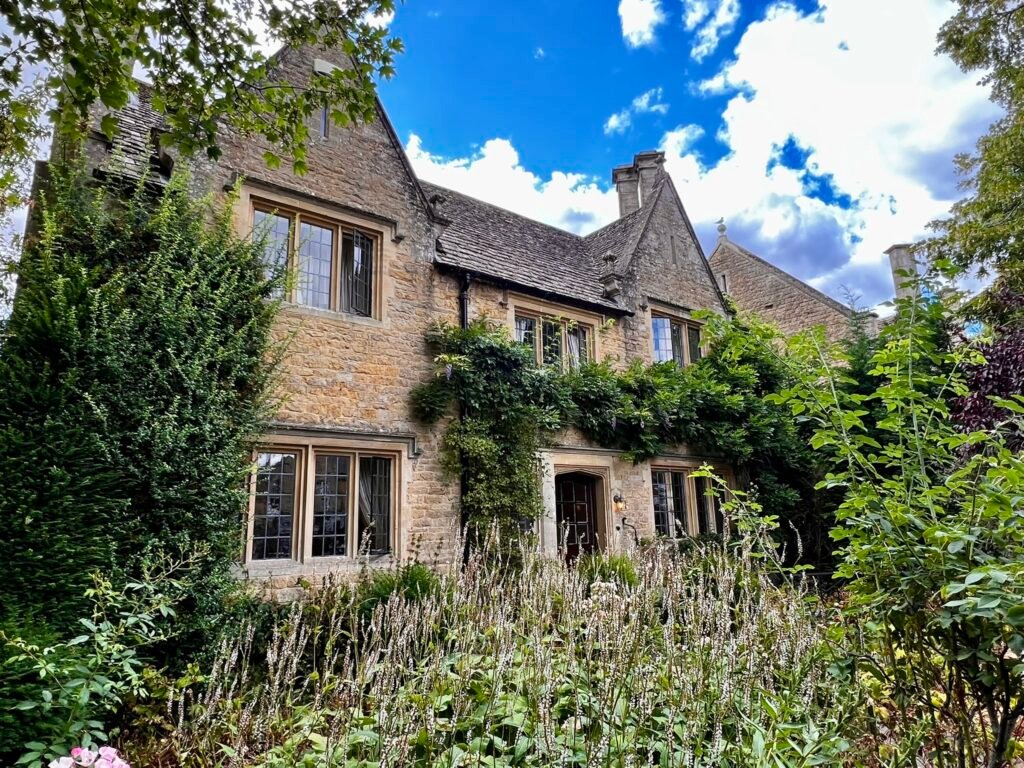 Traditional stone house surrounded by mature greenery and garden plants.