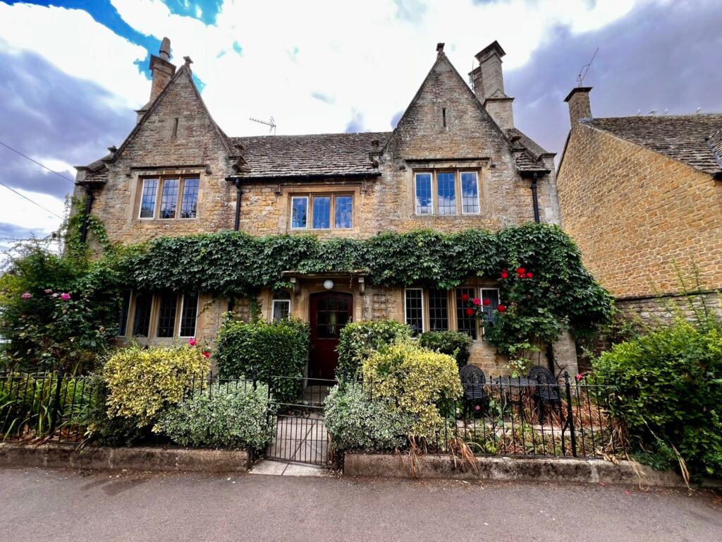 Cotswold stone house with twin gables, ivy, roses and a front garden.