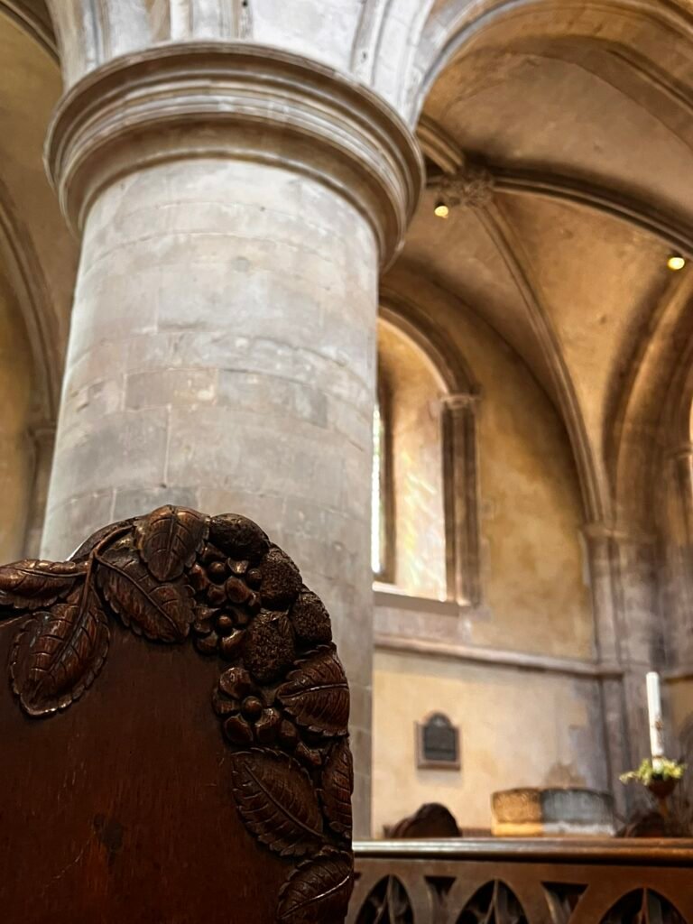 Intricately carved wooden pew end with leaves and berries inside the Church of St Cross.