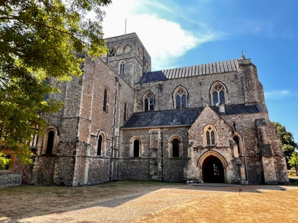 Side view of the Church of St Cross with its stone entrance, tower and flint walls.