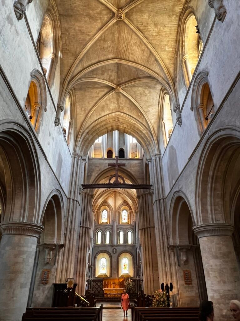 Tall stone arches, wooden pews and the long nave inside the Church of St Cross.