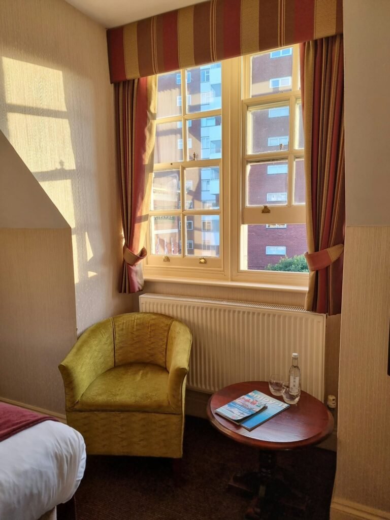 Hotel Miramar guest room with a bed, green armchair and sunlit sash window.