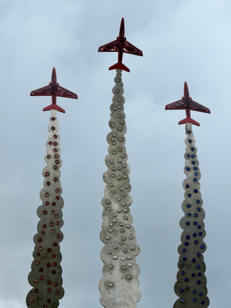 Three red aircraft above the coloured sculpted trails of the Jon Egging Memorial