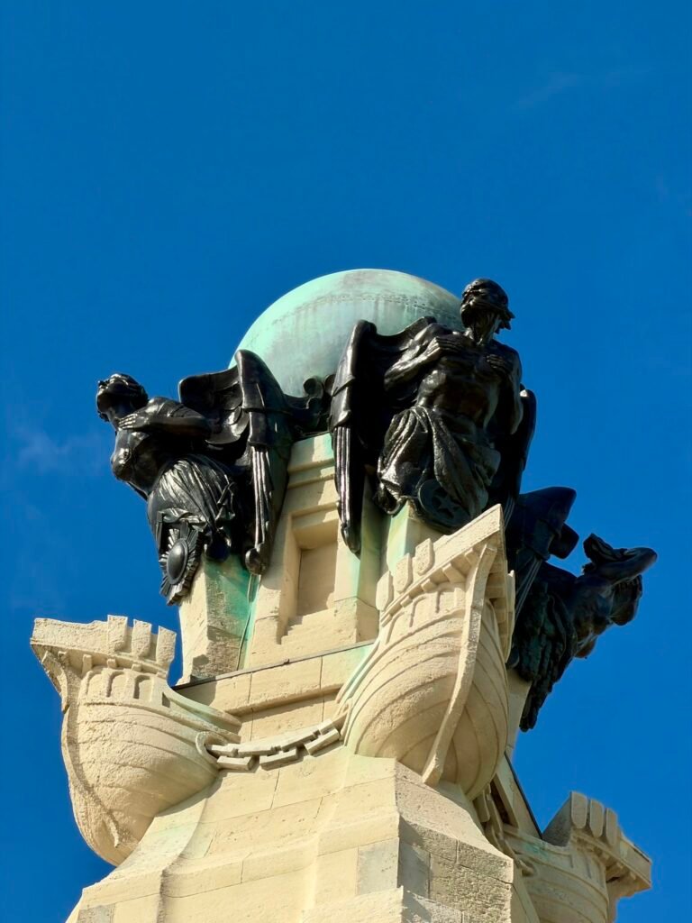 Bronze figures and green copper globe above carved ship prows at Portsmouth Naval Memorial