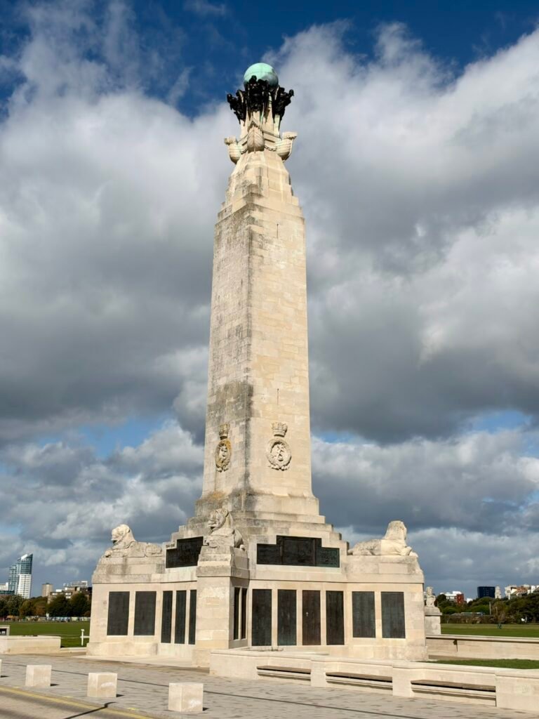 Tall stone obelisk at Portsmouth Naval Memorial with reclining lions and bronze panels