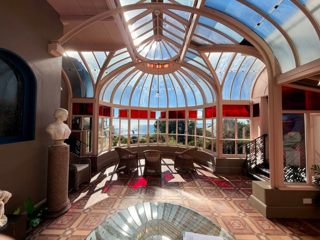 Curved glass-roofed conservatory with red glass panels and wicker chairs overlooking Bournemouth Bay