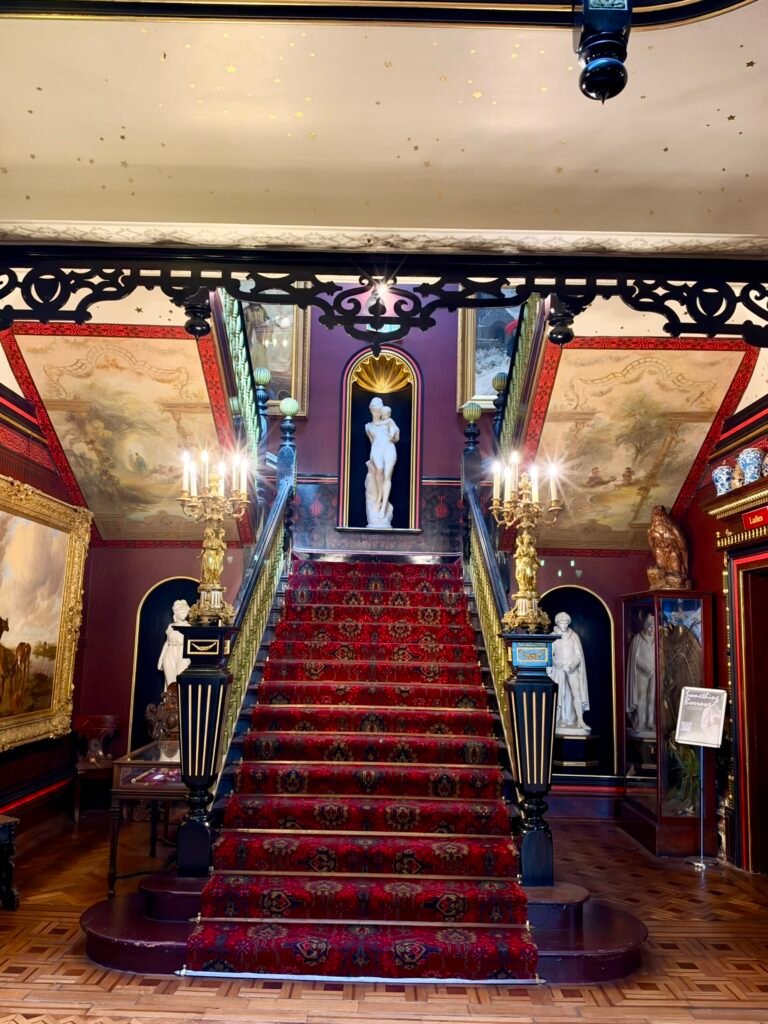 Red-carpeted double-return staircase with statues and ornate banisters Inside Russell-Cotes Museum