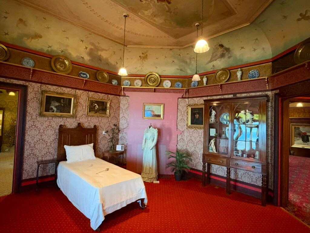 The Red Room at Russell-Cotes Museum with a single bed, red carpet and decorative ceiling