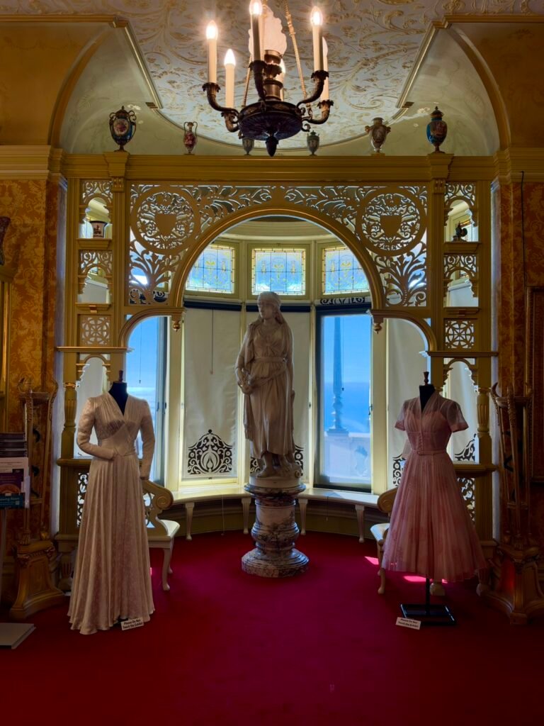 Two historic-style dresses beside a marble statue and carved screen in the Russell-Cotes Drawing Room