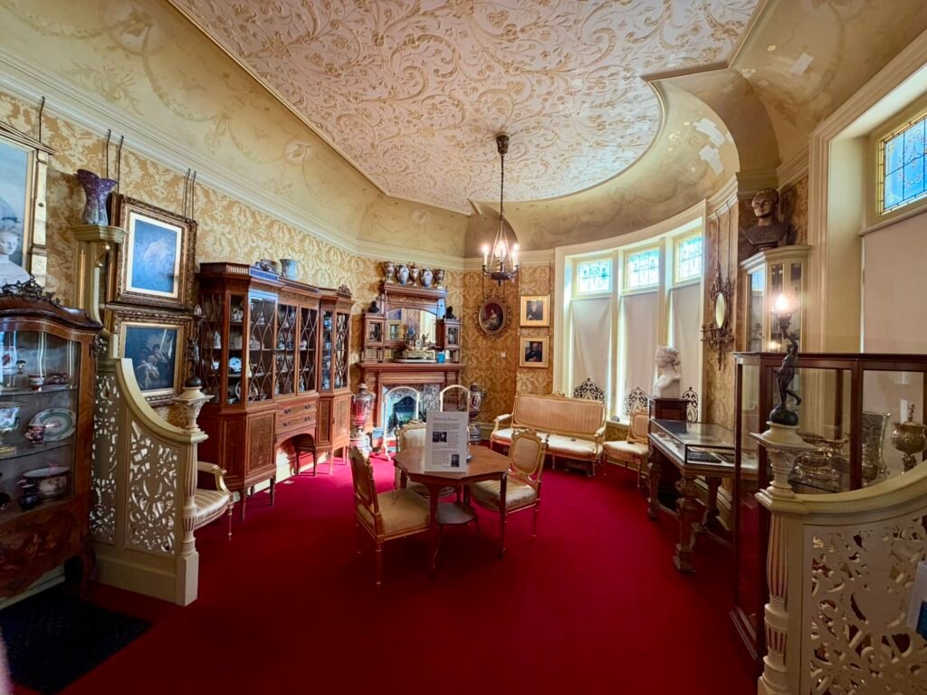The Russell-Cotes Drawing Room with ornate plaster ceiling, antique cabinets, gilt details and deep red carpet