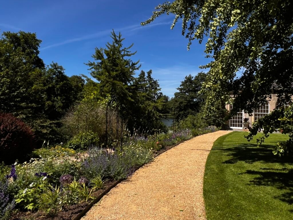 Curved gravel path beside colourful flowering borders and neatly mown lawn