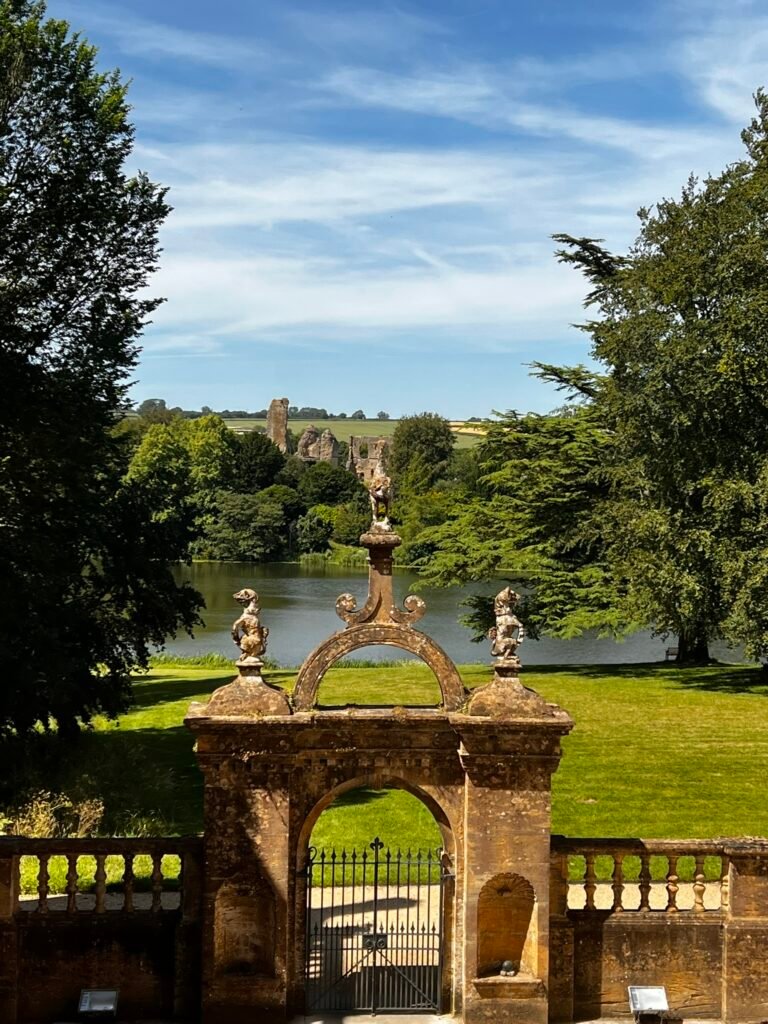 Ornate stone garden gateway with lake and Sherborne Old Castle ruins beyond
