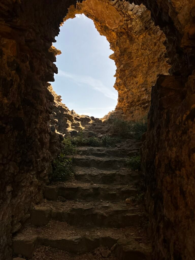 Dark stone steps rising through the ruins of Sherborne Old Castle towards daylight