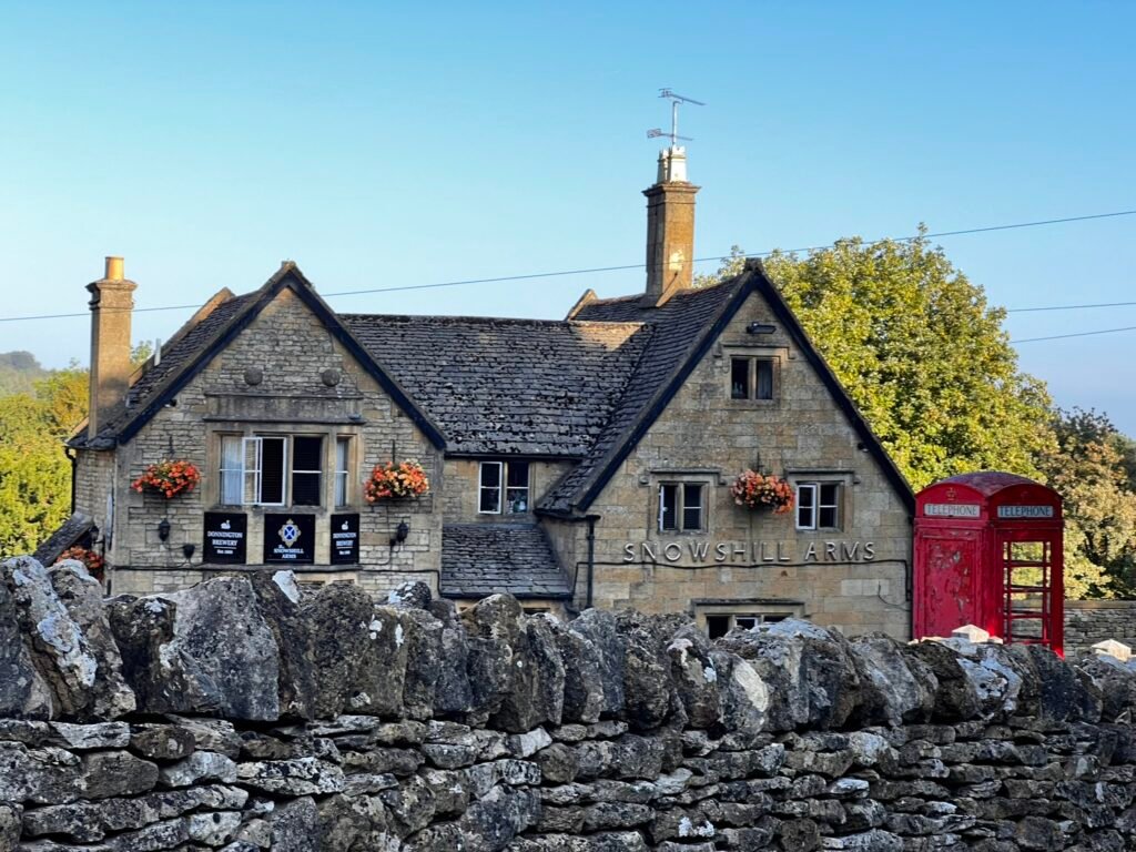 The Snowshill Arms pub beside a bright red British telephone box, behind a Cotswold stone wall.