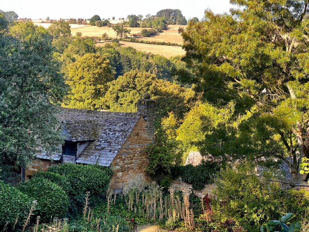 Old stone cottage surrounded by trees, with golden countryside stretching across the hills beyond.