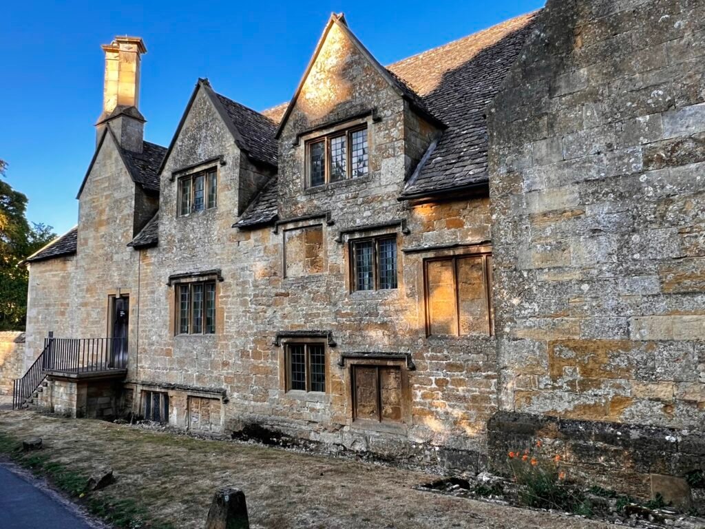 Historic stone building in Snowshill with steep gables, mullioned windows and tall chimney stacks.