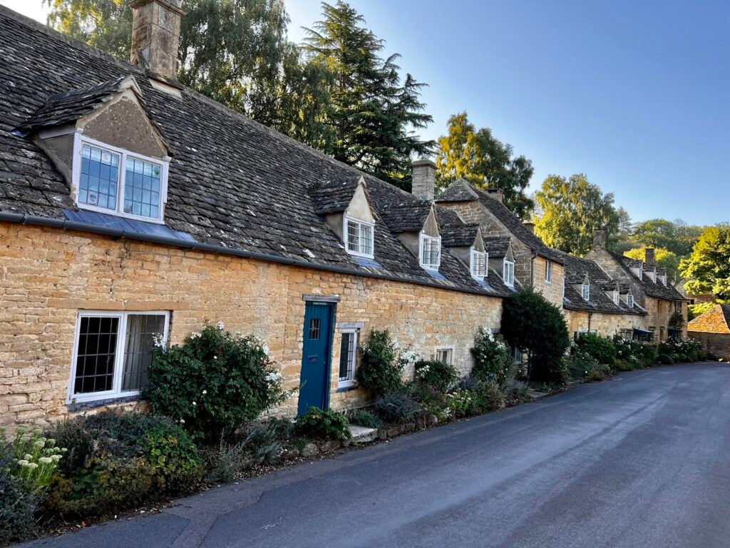 Row of honey-coloured stone cottages with dormer windows, flowers and a blue door in Snowshill.