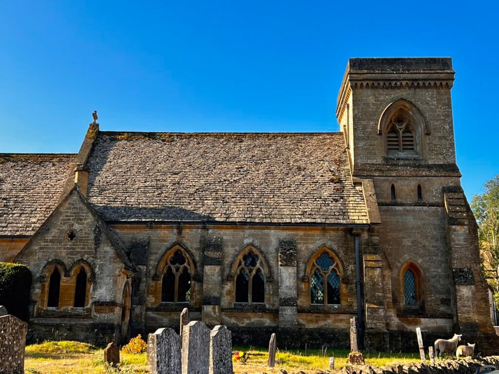St Barnabas Church in Snowshill, with its square stone tower, churchyard and surrounding hills.