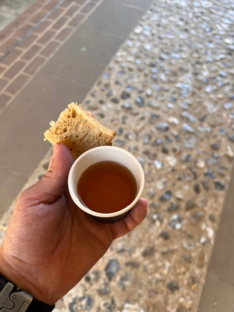Hand holding a small cup of ale and piece of bread received at the Hospital of St Cross.
