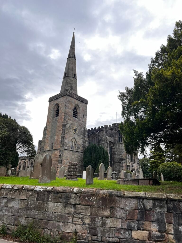 Old gravestones and stone boundary wall beside St Mary's Church in Astbury, Cheshire.