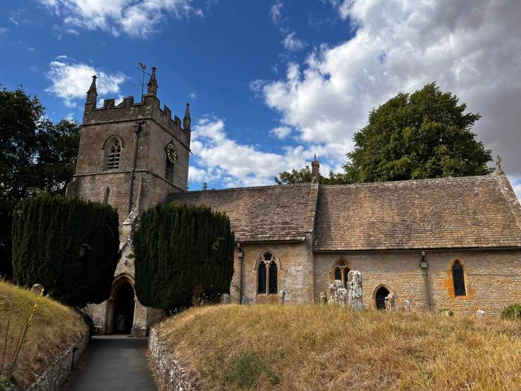 St Peter's Church, Upper Slaughter, with its stone tower, churchyard and sloping path.
