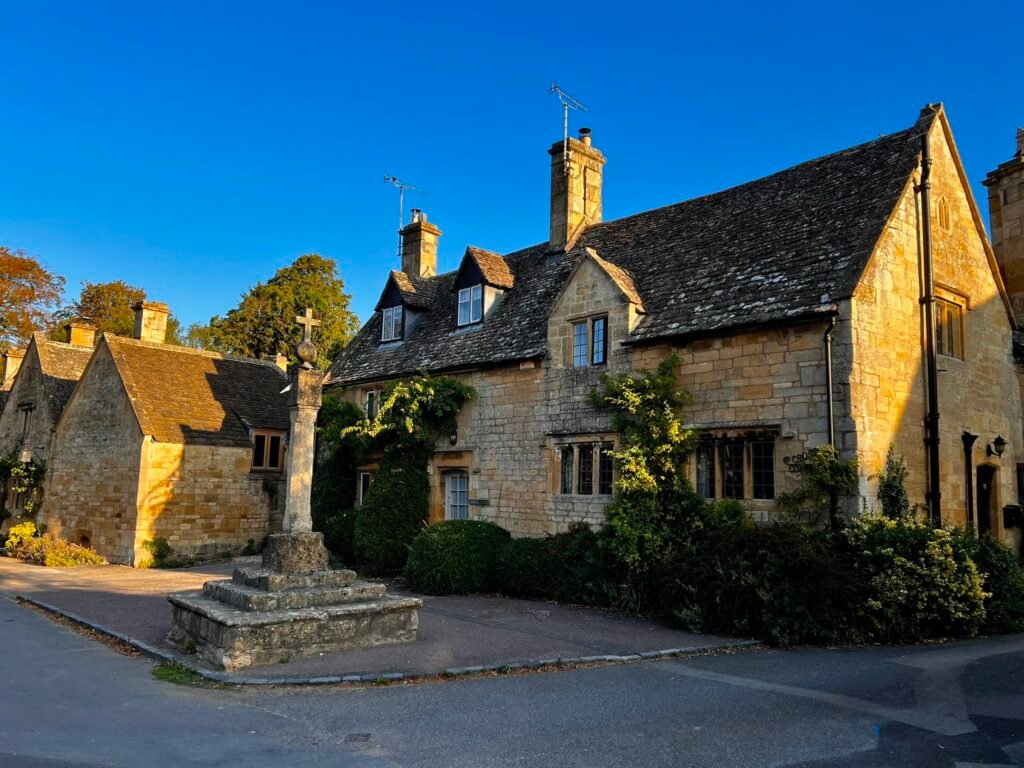 Historic stone village cross beside traditional Cotswold cottages in Stanton