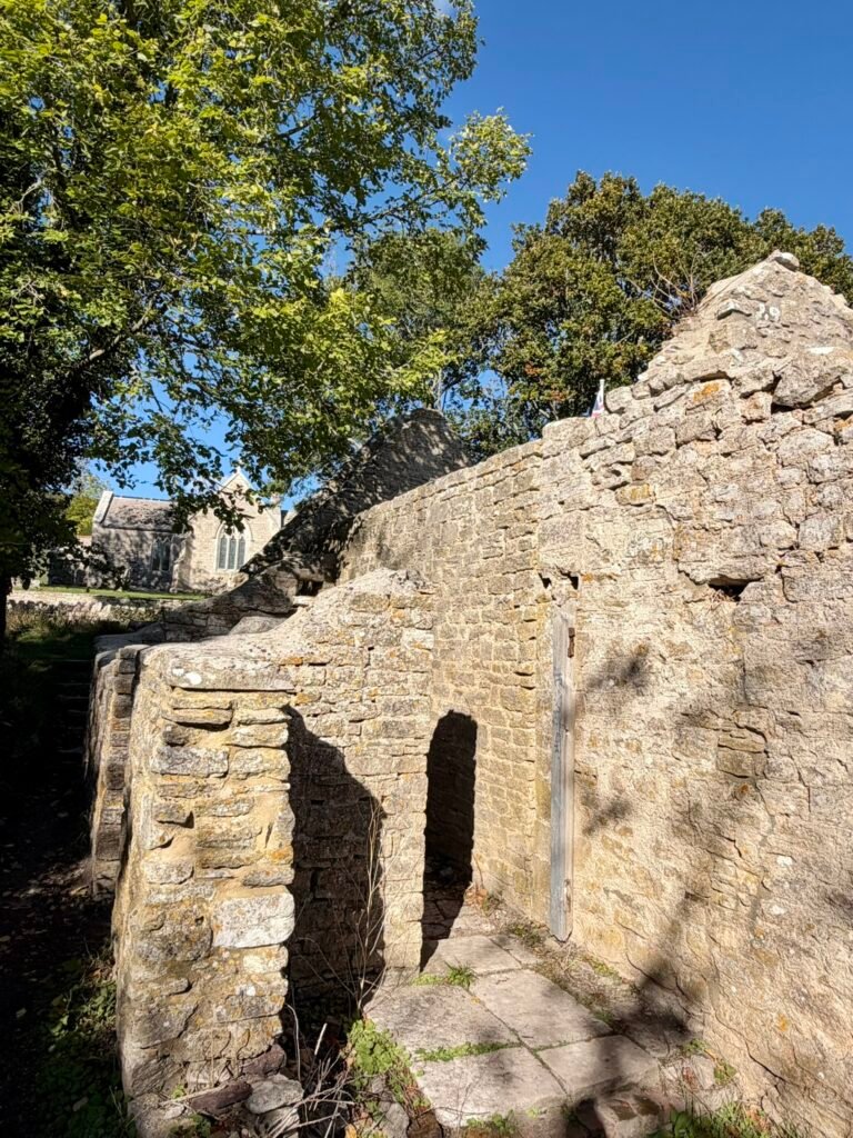 Ruined stone cottages in Tyneham village, Dorset, with St Mary’s Church beyond the walls