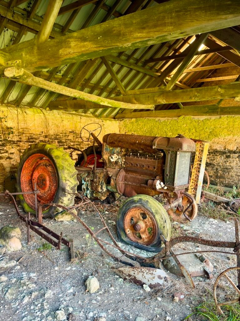 Rusting vintage tractor and old agricultural equipment inside a stone farm building at Tyneham