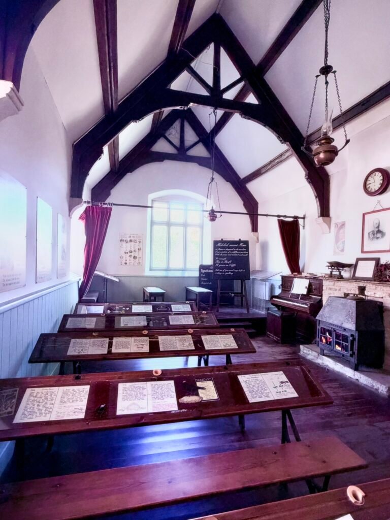 Interior of Tyneham School in Dorset, with timber roof beams, historical displays and a piano