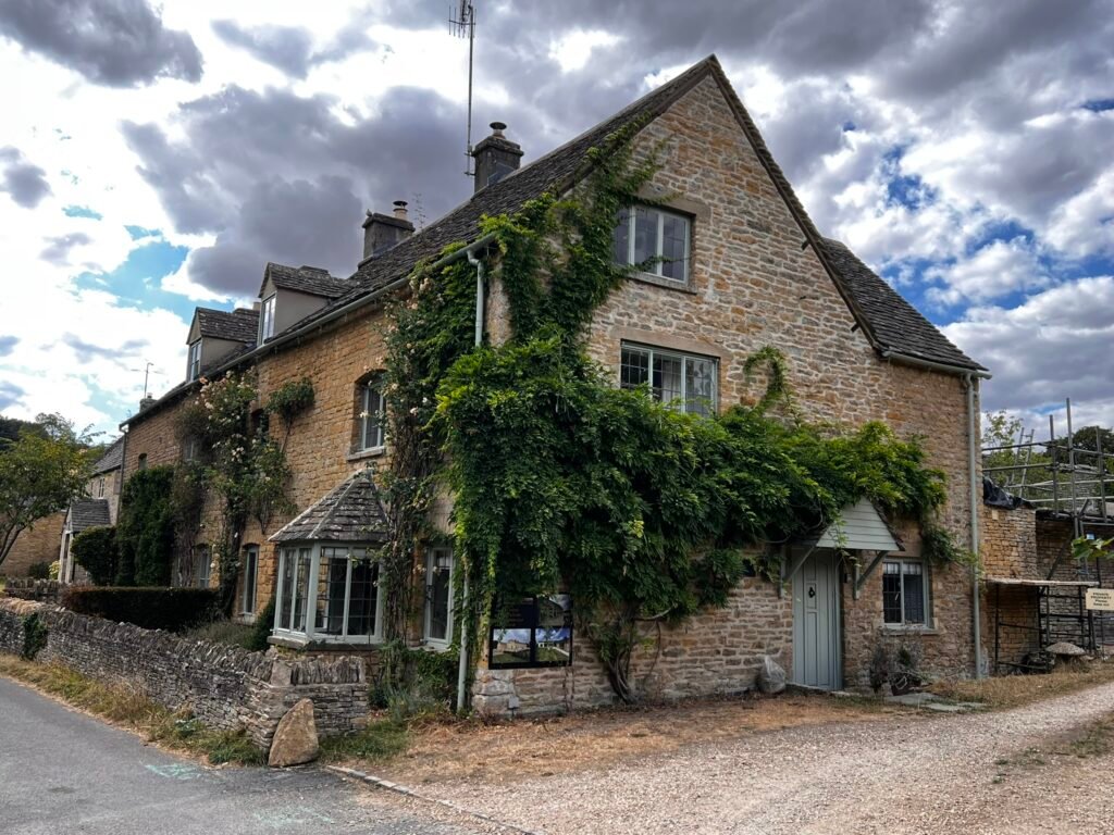 Large Cotswold stone house with climbing greenery and a steep tiled roof.
