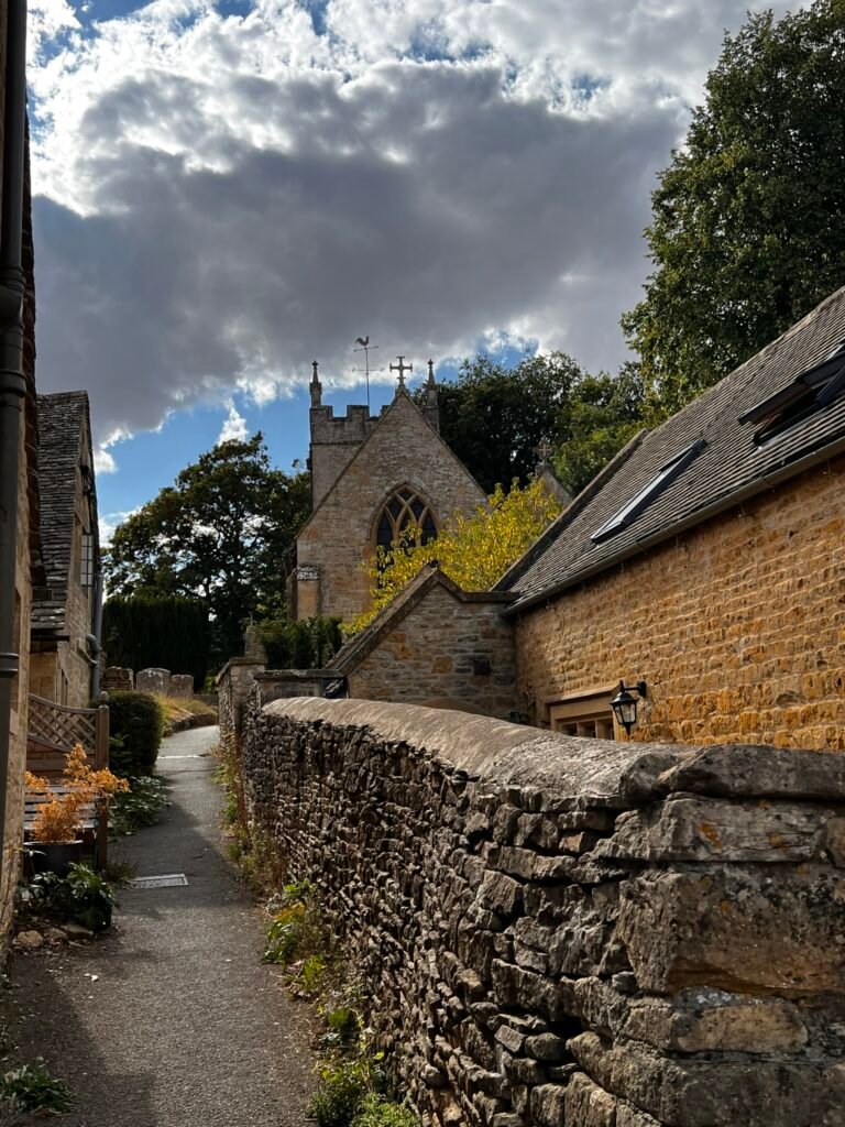 Narrow village footpath beside a stone wall leading towards St Peter's Church.
