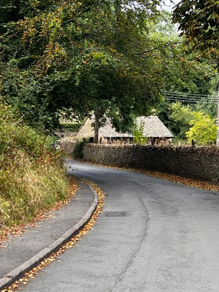 Narrow road curving beside a dry stone wall and trees in Upper Slaughter.